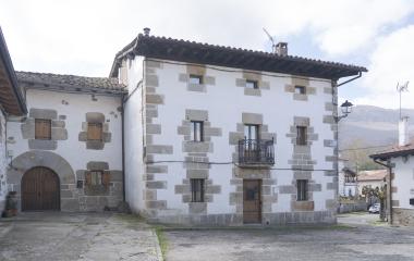 Casona de piedra y blanco en Iturmendi con fachada de sillería, ventanas alineadas y balcón de hierro forjado.