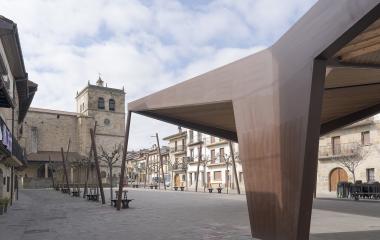Plaza de Lakuntza con iglesia de piedra, arquitectura tradicional y estructura moderna de madera y acero.