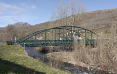 Puente de hierro verde sobre río en entorno rural con bosques y vegetación a ambos lados, a la entrada de Legasa.