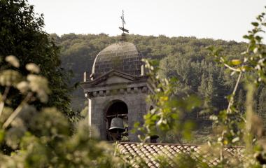 Campanario de piedra con cúpula en Leitza, rodeado de vegetación y bosque de fondo.