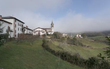 Casas vascas blancas con elementos arquitectónicos de piedra oscura, formando conjunto urbano y prados de alrededor en Lekaroz.