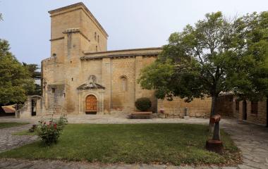 Iglesia de piedra arenisca en Lerga con torre cuadrada, portada y patio rodeado de vegetación.