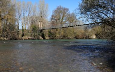 Puente colgante sobre río en Longuida con bosque y cielo despejado.