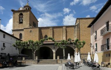 Iglesia de Lumbier con torre de reloj, campanario, claustro de arcos de piedra y plaza con terrazas.