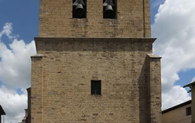 Torre campanario de piedra en iglesia de Lumbier, con dos campanas visibles.