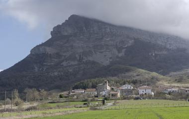 Valle de Ergoiena con iglesia al pie de montaña rocosa con niebla en cima.