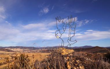 Escultura metálica de un ave en Peña Izaga con panorámica de valle y montañas al fondo.