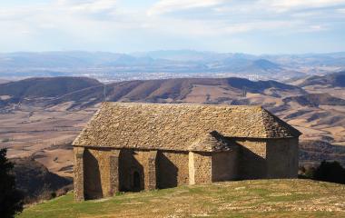 Ermitage en pierre sur une colline à la Peña Izaga, avec un paysage agricole et boisé en arrière-plan.