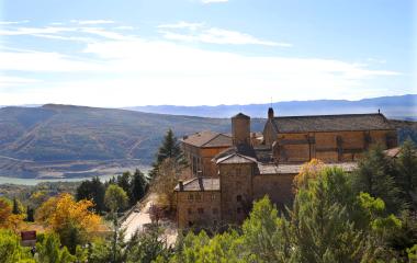 Monasterio medieval de piedra en Sierra de Leyre con valle y montañas al fondo.