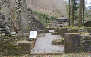 Ruinas de la Fábrica de Armas de Eugi integradas en bosque de hayas, con panel informacion y muros de piedra.