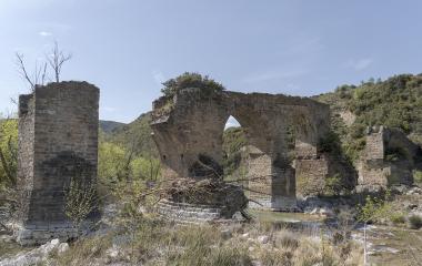 Ruinas de puente medieval con arcos de piedra sobre río en Puente de los Roncaleses, rodeado de vegetación y montaña.