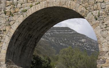 Stone arch of Puente de los Roncaleses framing a valley and mountains in the background.