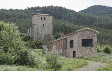 Palacio de Nagore con torre y campanario de piedra, rodeado de vegetacion y montañas boscosas.