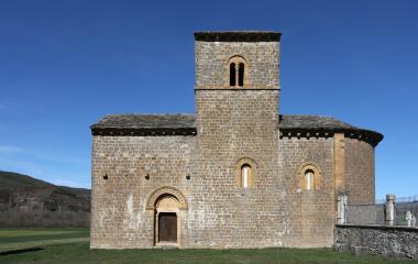 Iglesia románica de piedra en Navascués con torre campanario cuadrada y prado verde al frente bajo cielo despejado.