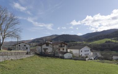 Casas dispersas en prado con montañas al fondo, paisaje rural típico de Baztan en Oitz.