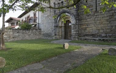 Iglesia de piedra con arco en Olloqui, Pirineo navarro, con camino de entrada y jardin bien cuidado.