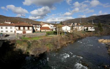 Pueblo de Oroz-Betelu junto al río con casas de piedra y tejados rojizos rodeados de montañas boscosas del Pirineo navarro.