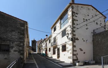 Calle empedrada de Petilla de Aragón con casas de piedra blanca y torre iglesia al fondo.