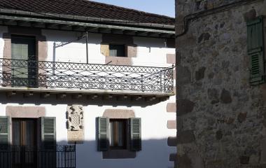 Fachada blanca con balcón de hierro y detalles rústicos de piedra.