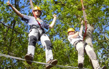 Deux participants sur un parcours aérien suspendus entre des arbres avec un harnais et un casque de sécurité à Bertiz Abentura Park, Baztan-Bidasoa.
