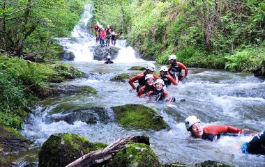 Descente de canyon en rivière avec des participants en combinaison de néoprène rouge et casque blanc, forêt atlantique dense et cascade en arrière-plan à Bertiz Abentura Park, Baztán Bidasoa.