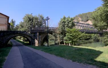 Paseo Cantolagua en Sangüesa con vía verde ribereña y puente de Sangüesa sobre río Aragón flanqueado por vegetación fluvial.