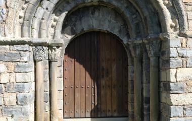 Portada románica de la Ermita de Santa María de Arce con arquivoltas de medio punto y puerta de madera oscura en piedra caliza, en Pirineo navarro.