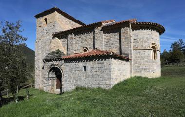 Ermita románica de Santa María de Arce en el Pirineo navarro, iglesia de piedra con torre campanario, rodeada de prado.