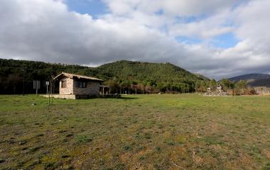Casa de piedra pequeña junto a prado en el valle del Pantano de Nagore, Pirineo de Navarra, con bosque de montaña al fondo.
