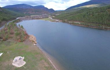 Embalse de Nagore en el Pirineo Navarro rodeado de bosque de coníferas y montañas calizas, con carretera y prados de fondo.