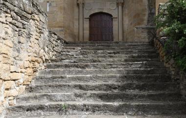 Escaleras de piedra ascendiendo hacia portada con arco en iglesia de San Vicente en Sada.
