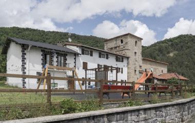 Conjunto de casas e iglesia con monte boscoso de fondo y un parque infantil en primer plano en Saigots.