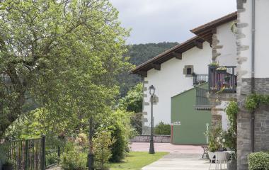 Calle de Saigots con casas a un lado y al otro vegetacion, al fondo se puede apreciar parte de un fronton.