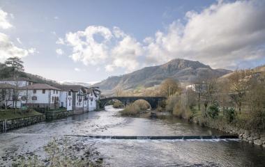 Vistas de Sumbilla desde el río mostrando casas blancas de arquitectura vasca, puente medieval y vegetación otoñal en monte de fondo.