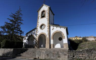 Iglesia de Unciti con torre campanario blanca y piedra, bajo cielo azul despejado.