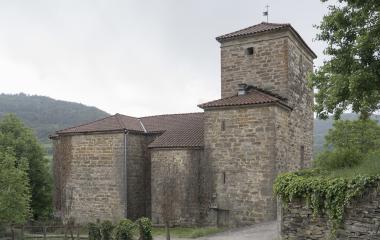 Iglesia rural de piedra en Urdaniz, Pirineo navarro, con torre cuadrada, rodeada de vegetación.