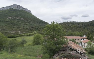Caserio tradicional de piedra, prado verde, monte boscoso y cortado calcareo al fondo en Urdiroz, Pirineo navarro.
