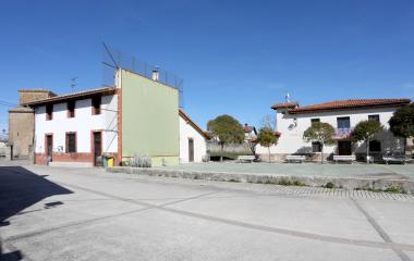 Plaza de Urraul Bajo con fronton de una pared verde, casas blancas y tejados de barro bajo cielo despejado.