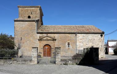 Iglesia de piedra con torre cuadrada en Urraul Bajo, fachada románica y puerta ojival bajo cielo despejado.