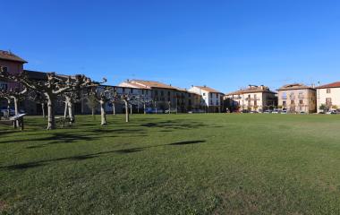 Jardin verde de Urroz-Villa con casas de piedra al fondo y árboles bajo cielo despejado.