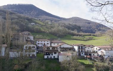 Paisaje panorámico del pueblo de Urroz rodeado de montañas verdes y casas dispersas en el valle.