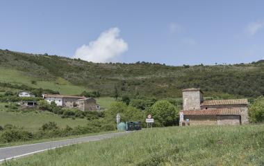 Entrada al pueblo de Usetxi con Iglesia de piedra, rodeada de prados verdes, montes boscosos y casas al fondo.