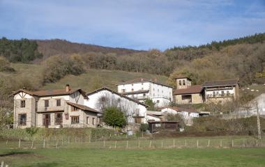 Conjunto de casas tradicionales de piedra y blanco en Imoz, rodeados de prados y bosques de montaña en otoño.