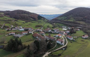 Vista aérea del Valle de Larraun con casas dispersas, prados verdes y bosques de montaña al fondo.