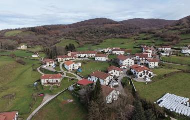 Vista aérea del Valle de Larraun con casas dispersas, prados verdes y bosques de montaña al fondo.
