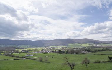 Pueblos de Valle de Ultzama con iglesia campanario rodeado de prados verdes y bosques de montaña al fondo.