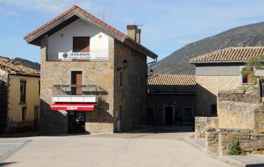 Albergue de piedra en Yesa con cartel identificativo, rodeado de arquitectura tradicional y montes al fondo.