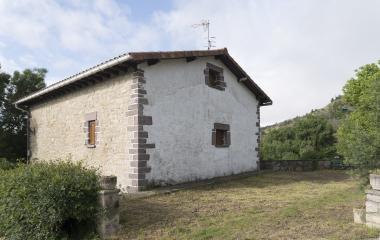 Casa tradicional de piedra blanca con esquinales de sillería en Zabaldika, rodeada de bosque.