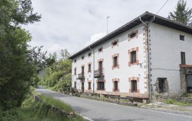Casa tradicional en Zandueta con fachada blanca de piedra en entorno boscoso.