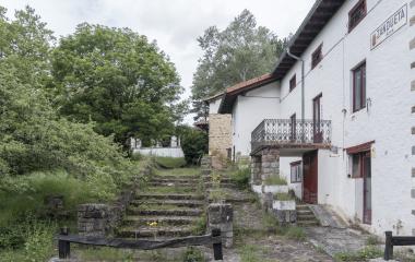 Casas tradicionales de Zandueta con fachada blanca, balconada de hierro y escalinata de piedra en entorno boscoso.